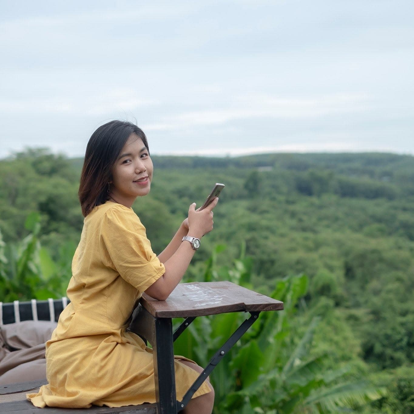 Nok in a yellow dress, smiling, with green hills behind